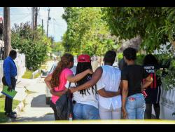 Family members huddle outside the Braeton, Portmore, home where Sonia Labeach Dillon was hacked to death and her daughter injured during Tuesday morning’s brutal attack.
