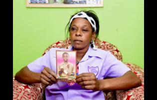 A mourning Stacy-Ann Dunkley wears the uniform shirt of her son Raniel Plummer, while displaying his photo.