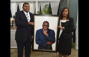 Karen Smith (right), the widow of Anthony Smith, and her son Daniel Smith (left), hold a picture of the late CEO of the RJRGLEANER Communications Group, during a thanksgiving service for his life on Sunday at the Karl Hendrickson Auditorium at Jamaica College.