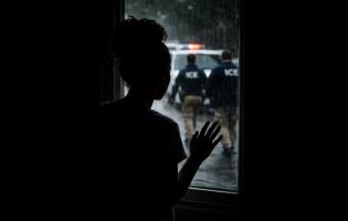 In this AI-generated image, Jane* stands at a window watching ICE agents outside, symbolising the fear and uncertainty faced by undocumented immigrants as court hearings approach and the threat of deportation looms.