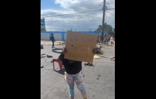 A resident of Jones Town bears a placard calling for justice for former footballer Lucien Anderson who was killed in an alleged confrontation with police on Sunday. The protest was on Slipe Pen Road in Kingston yesterday.