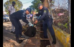 Police Inspectors Heather Mclean (left) and Hugh Lewis of the Constant Spring Police Station, clear leaves and other debris from a drain at the Constant Spring Police Station during a clean-up activity at the station grounds in St. Andrew on Saturday (February 21). The exercise involved partnership with the National Solid Waste Management Authority (NSWMA). 

