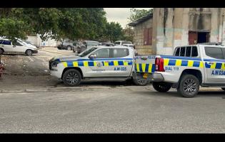 Parking lot adjacent KPH filled with vehicles, now cordoned off. Pedestrian access restricted as the police process the scene.