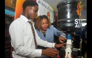 Education Minister Senator Dr Dana Morris Dixon (second left) examines an automatic chicken feeder made by students of St Andrew Technical High School, during an alumni engagement visit on Tuesday, in commemoration of the institution’s 65th anniversary. Explaining how the device functions is grade 11 student, Cameron Pinnock (left). Looking on is principal, Dr Worrel Hibbert (partially hidden).