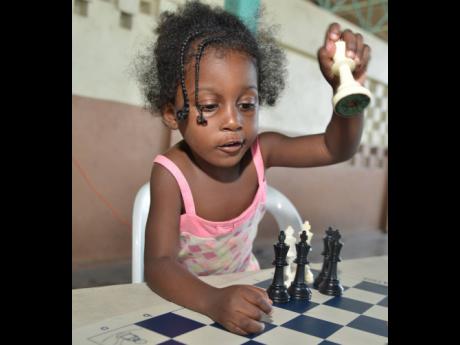 Three-year-old Tajarie Hayden from the Denham Town community makes a chess move.