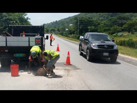 Several workmen contracted to the National Works Agency carry out repair work yesterday on the section of roadway in Barbican, Hanover where popular Lucea bus operator Everton ‘Wanga’ Riley, and Kevaughn Sutherland lost their lives in a motor vehicle accident, on Wednesday.