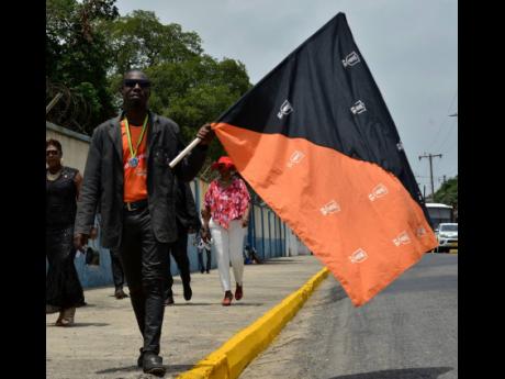 Rohan Banner carries a flag which represents the Tivoli Gardens Football Club as he attends the state funeral of the former Club President and Prime Minister Edward Seaga yesterday.