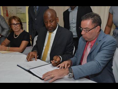 Daryl Vaz (right), minister without portfolio, in the Ministry of Economic Growth and Job Creation, signs the contract with Enterprise Electronics Corporation for the installation of a new Weather Radar System for Jamaica, with Dr Wayne Henry, director general of the Planning Institute Of Jamaica. 