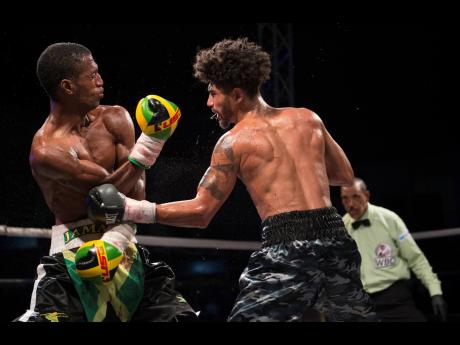 Toriano Nicholas (left) of Jamaica receives a hard left to the body by American boxer Carlos Dixon during the Gloves Over Guns fight night held at the Ambassador Theatre in Trench Town, Kingston, on Saturday, July 13. 