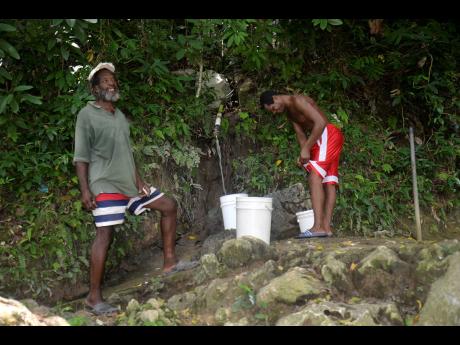Billy (left) and Neville, two residents of  St Simon, also known as Fat Hog’s Quarters in Hanover, catch water at a spring in the community .