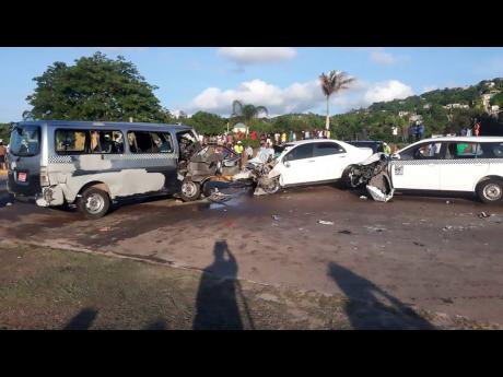 Onlookers view the crash scene in Montego Bay yesterday. Two of the drivers were killed.