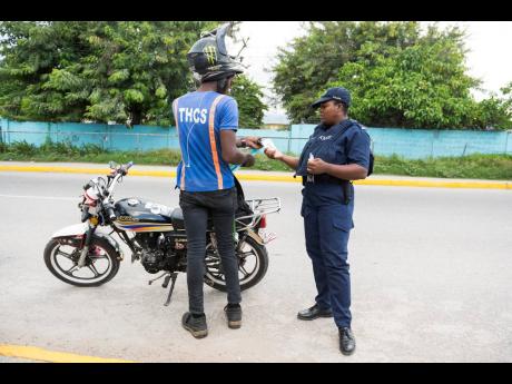 A policewoman checks the ID of a motorcycle operator along Olympic Way yesterday in the vicinity of the White Wing community.