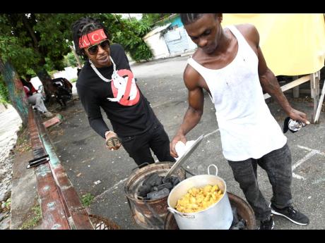 Savage’s childhood friend, Kemar Smith, aka ‘Famo’, checks on the pot while the deejay looks on.