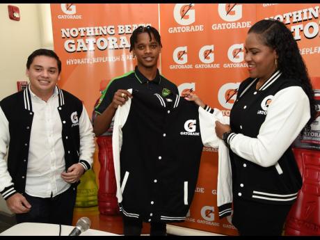 Credit: Ian Allen Peter-Lee Vassell (centre) displays a Gatorade jacket shortly after signing a two-year contract to become a brand ambassador for Gatorade Jamaica. Looking on are Michael Castillo (left), commercial director, and Cornelia Nathan, brand manager, both of Gatorade, Jamaica.
