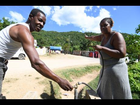 Wilburn Forbes and Susan Morgan show a pipe which gets water from the tank beside the community centre.