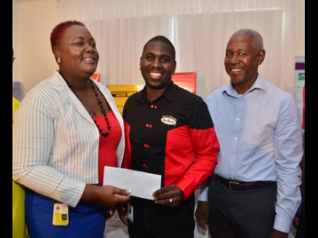 Promotions manager at Grace Kennedy, Ricardo Smith (centre), presents a sponsorship cheque to meet chairman Camille Allen during the launch of the 2020 Camperdown Classic at the Spanish Court hotel  yesterday. Looking on is Peter Hibbert, the former Camperdown High sprinter, who will be this year’s honouree. 