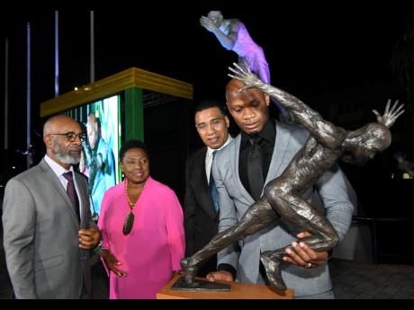 Asafa Powell (right) inspects the bust of a sculpture of himself in Statue Park at Independence Park yesterday as (from left) sculptor Basil Watson, Minister of Sport, Olivia Grange, and Prime Minister Andrew Holness look on.
