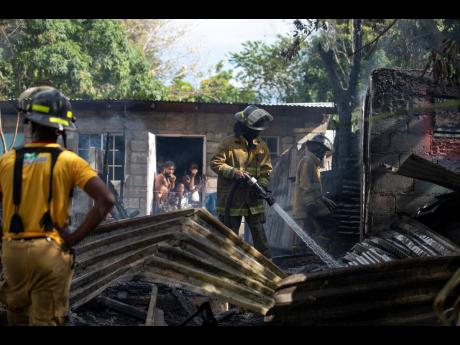 Firefighters perform cooling-down operation after in Vietnam, an area located off Grants Pen Drive in St Anrdew, where three houses were destroyed yesterday.