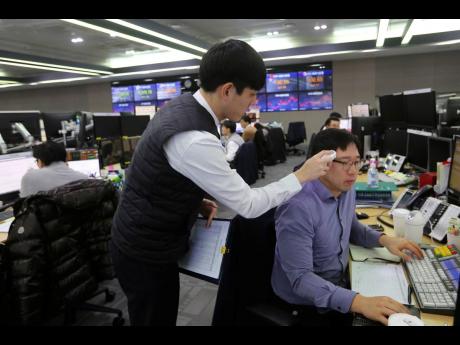 A currency trader checks the temperature of his colleague at the foreign exchange dealing room of the KEB Hana Bank headquarters in Seoul, South Korea, on Thursday. Asian shares were mixed Thursday after Wall Street recovered to record highs, but worries continued about the damage to the regional economy from the new virus that began in China.