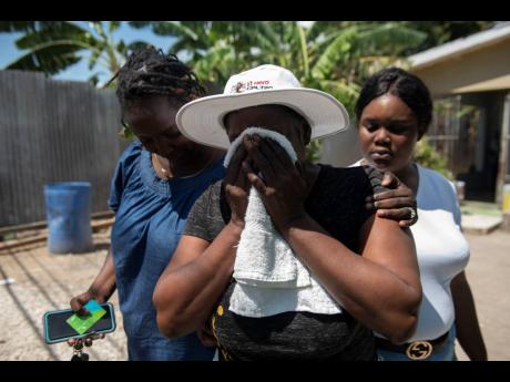 Marjorie Powell (centre) is overcome with grief as she mourns the loss of her son Irvino English, a former national football player. Powell is consoled by Tina Palmer (left) and Alicia Breakenridge.