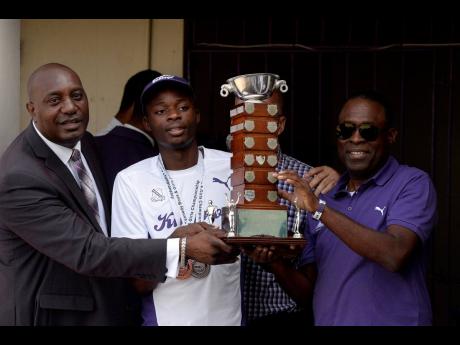 Credit: Lionel Rookwood From left: David Myrie, principal, Kingston College,Tarees Rhoden, captain, track team and head coach, Leaford Grant present The Mortimer Geddes trophy for Inter-Secondary Schools Athletics to the school during a Champs Celebration held at Kingston College on April 1, 2019.