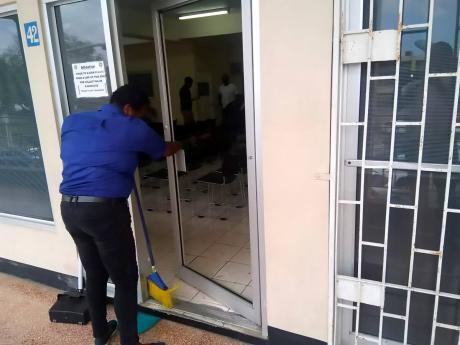 An employee at the passport office in Montego Bay sweeps up broken glass, after a security guard broke through the door, and then drank several substances from a nearby pharmacy. 