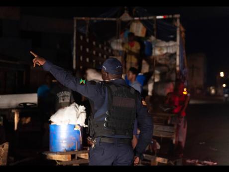 A member of the Jamaica Constabulary Force reprimands a group of men who were  unloading farm produce at the Coronation Market in downtown Kingston on Wednesday during the time of the islandwide curfew.