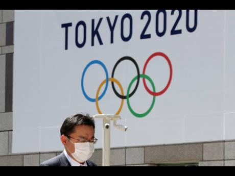  In this Wednesday, March 25, 2020, file photo, a masked man walks in front of a Tokyo Olympics logo at the Tokyo metropolitan government headquarters building in Tokyo. The Tokyo Olympics have been moved to next year. But countless questions remain. They revolve around 11,000 Olympic athletes and 4,400 Paralympic athletes. They also include 206 national Olympic committees, sports federations, thousands of contracts, and billions of dollars.