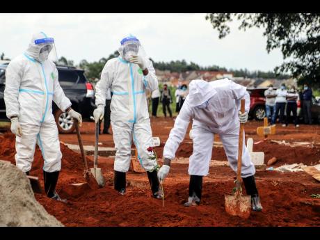 Public health officers wearing protective clothing at the grave site of a man who died from the coronavirus in Nairobi, Kenya. Attendance at funerals in Jamaica and much of the world are now being attended by a small number of persons, a measure instituted to slow the spread of the virus.