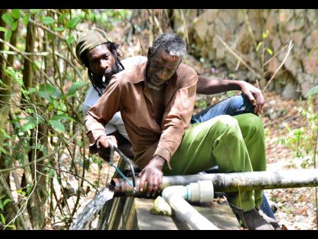 Gladstone Ewart (front) and Derventt Henry repair a pipe that takes water to their farms at Coptic in St Thomas.