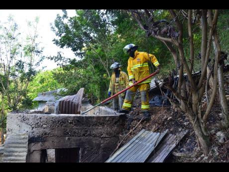 Firefighters conduct cooling down operation at this house in Burnside Valley, Red Hills, St Andrew, yesterday.