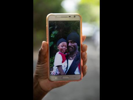A photo of Kimani Taylor with son Tyler is shown on a cell phone in the vicinity of where three burnt bodies were found on Sunday. Taylor’s family are convinced that he and his son, along with Lexton Clayon, have met a tragic end.