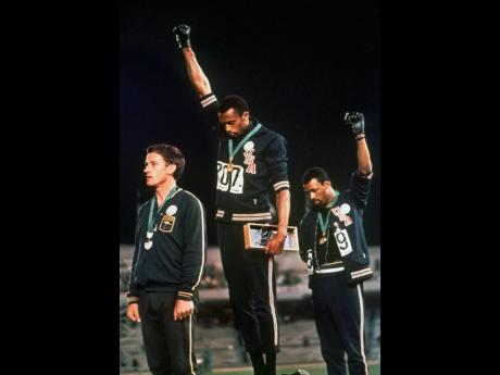 In this file photo from October 1968, United States athletes Tommie Smith (center) and John Carlos (right) stare downward while extending gloved hands skyward during the playing of the American national anthem after Smith received the gold, and Carlos the bronze medal, for the men’s 200m sprint at the Summer Olympic Games in Mexico City, Mexico. Australian silver medalist Peter Norman is at left. The Americans were using their international platform to protest for black civil rights back home.