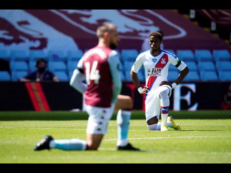 Crystal Palace’s Wilfried Zaha takes a knee in support of the Black Lives Matter movement before the English Premier League match between Aston Villa and Crystal Palace at Villa Park in Birmingham, England, Sunday, July 12, 2020.