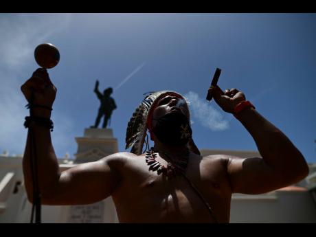 Gypsy Cordova blows smoke and shakes a maraca in front of a Juan Ponce de Leon monument while leading a group of activists in a march demanding statues and street names commemorating symbols of colonial oppression be removed, in San Juan, Puerto Rico on Saturday, July 11. Dozens of activists marched through the historic part of Puerto Rico’s capital on Saturday to demand that the U.S. territory’s government start by removing statues, including those of explorer Christopher Columbus.