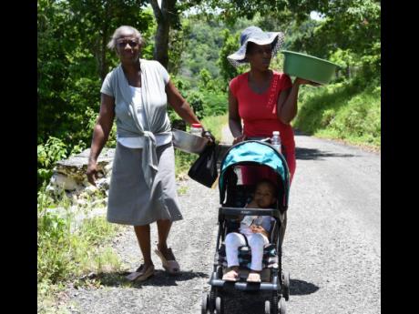 Brenda Simms (left), her daughter Nackiesha Robinson (right), and baby Amora Cramwell walk home from their field in Sturge Town, St Ann, on Tuesday.