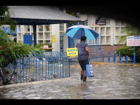 A pedestrian wades through water in front of the Jamaica National Bank outlet on Constant Spring Road on Thursday as heavy rains associated with a tropical depression lashed parts of the island.