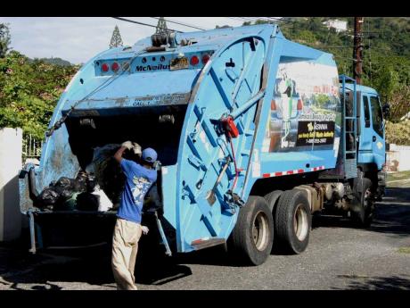 A member of the work crew puts domestic waste in the back of a National Solid Waste Management Authority compactor truck.