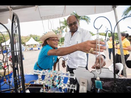 Denise Wedderburn assists Tourism Minister Edmund Bartlett as he browses craft jewellery at the Treasure Beach Benevolent Society booth at the Christmas Craft Fair, held at Emancipation Park in St Andrew last December. 
