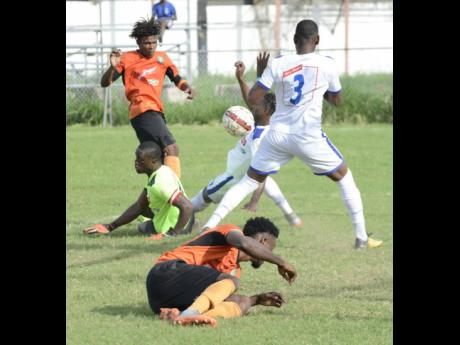 Lynval Wilson (right) from Reno FC blocks a ball heading towards goal from Ramaine Brakenridge (left) from Tivoli Gardens FC after Dennis Taylor  (second left) was left beaten on the ground in a 2018 Premier League match.  Also on the ground is Tivoli’s Andre Moulton.