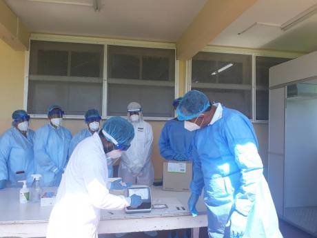 Medical technologist Shaemar Wiles (left) preparing to test a sample for COVID-19 using one of the rapid antigen test kits. Looking on is Health Minister Dr Christopher Tufton.