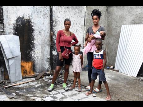Peta-Gay Martin and members of her family, stands in the shell of their house that was destroyed by fire in May. The mother of six is seeking to have it rebuilt.