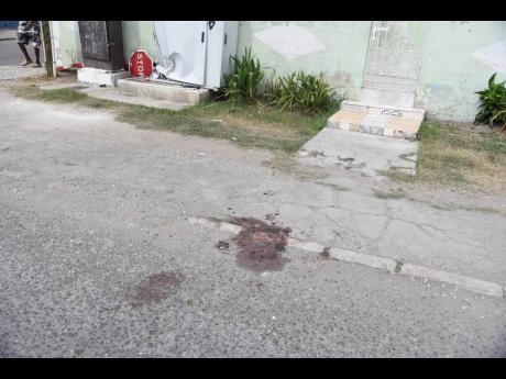Blood stains the sidewalk where three men were shot in Arnett Gardens on Monday afternoon.