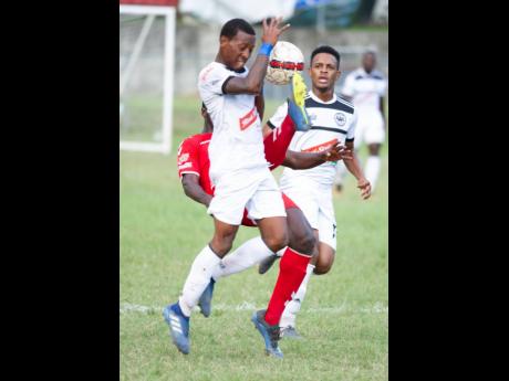 Cavalier’s  Chevonne Marsh takes evasive action from a tackle by UWI’s Tejuran Williams, who attempts to clear the ball as Alex Marshall looks on, during a Red Stripe Premier League match on December 2, 2018. 