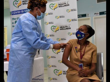 Public health nurse Fiona Ellis (left) administers the COVID-19 vaccine to senior nurse Marcia Thompson-Yetman, making her the first person in Jamaica to get the jab.