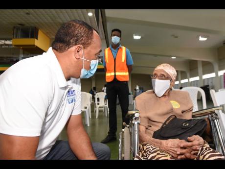 Minister of Health, Dr Christopher Tufton, speaks with 104-year-old Hazel Espuet during a vaccination exercise at the National Arena in Kingston on April 3.