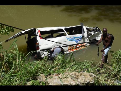 Divers attempt to attach cables to the ill-fated mini bus in order for the wrecker to lift it from the Rio Cobre.