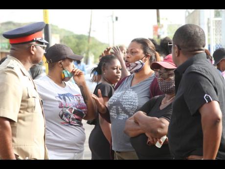 These persons get the ears of a senior policeman as they protest an incident that led to the deaths of three youngsters and the injuring of five others in Lionel Town, Clarendon.