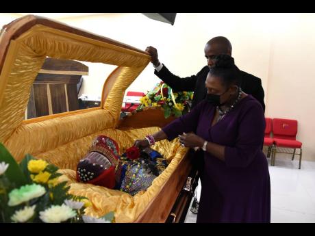 Culture Minister Olivia Grange places a rose on the body of Lee ‘Scratch’ Perry at Perry’s Funeral Home yesterday in St Catherine. Looking on is Peter Perry, CEO of the funeral home. The body was later transported to Hanover for burial.