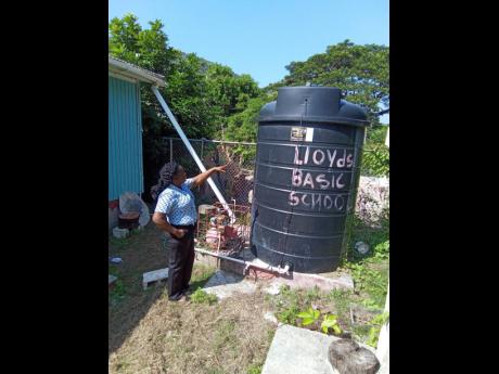 Elesha Cuthbert, principal of Lloyds Basic School in St Thomas, points to the water tank on which the school relies to maintain proper sanitation at the institution. A water pump on which the tank relied stopped functioning, and the institution has not been able to acquire another. With help from JN Money, it will rehabilitate the concrete platform on which the tank now sits to rely on gravity feed.